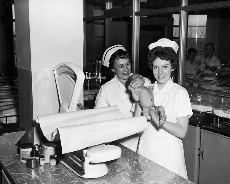 Two nurses with baby in nursery at Toronto East General and Orthopaedic Hospital, Toronto, ON