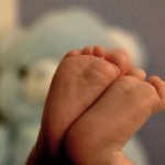 A close of of tiny baby feet with a teddy bear in the background